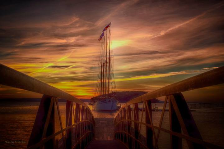 Sailboat docked at sunset viewed from a pier, with vibrant sky.