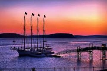Sunset over a harbor with sailboats and a pier in silhouette.