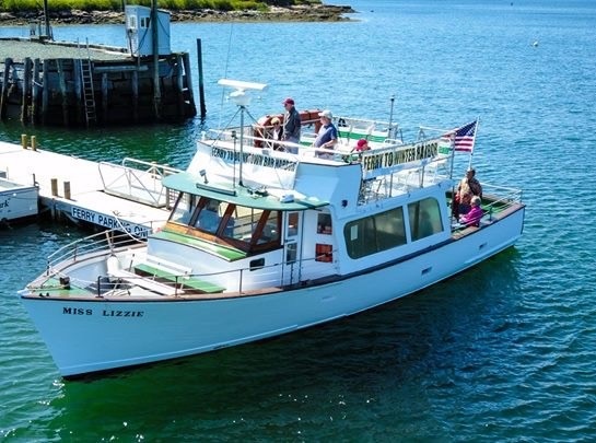 Boat named 'Miss Lizzie' docked with passengers onboard, American flag on stern, sunny day.