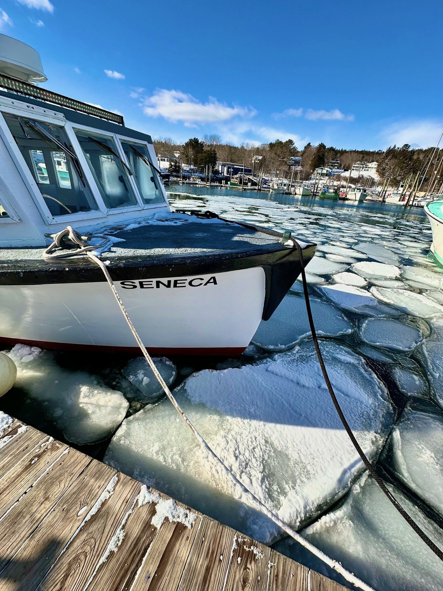 Boat named Seneca docked on icy water under blue sky in a snowy marina.