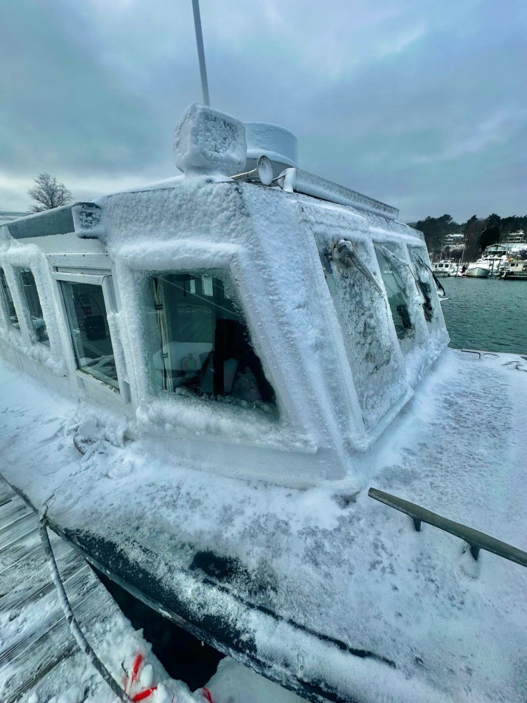 A boat covered in ice and snow docked at a frozen snowy pier.