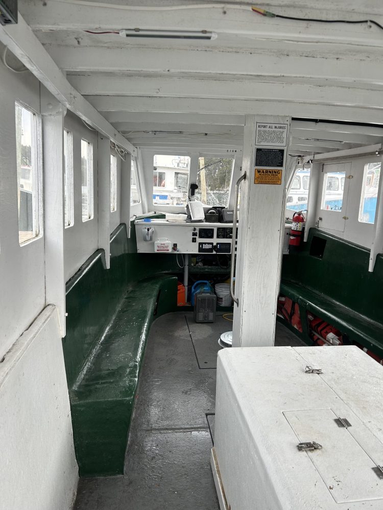 Interior of a small boat with green benches and equipment on the deck.