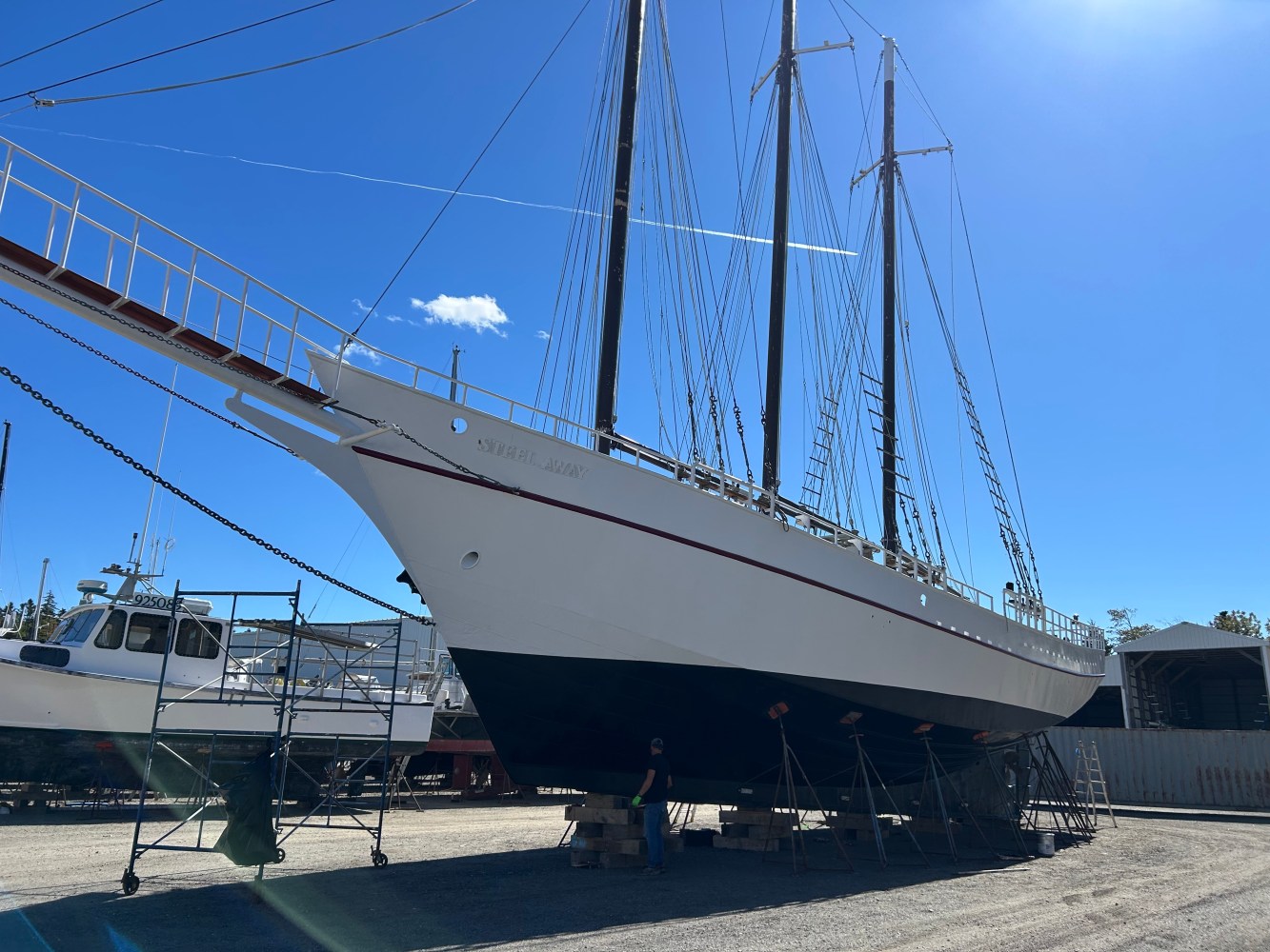 Large sailboat on dry dock with blue sky and other boats nearby.