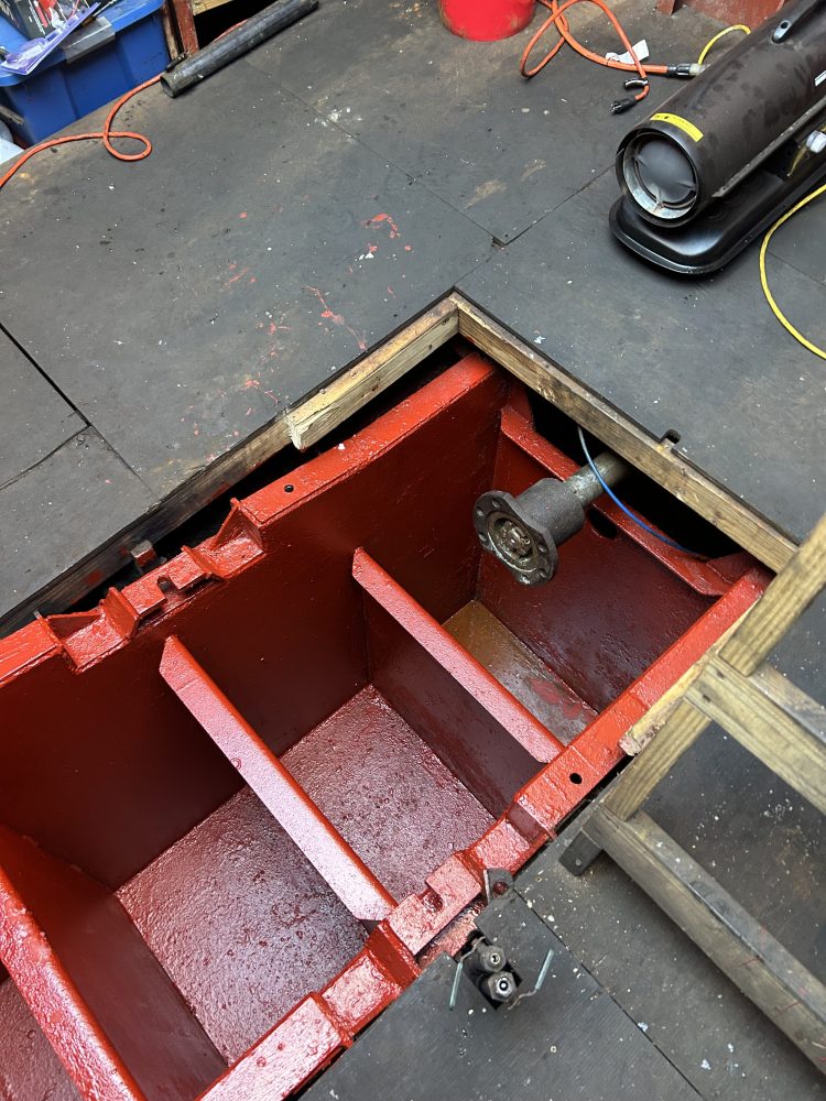 Red-painted compartment on floor with wooden cover, electrical cords, and tools around.