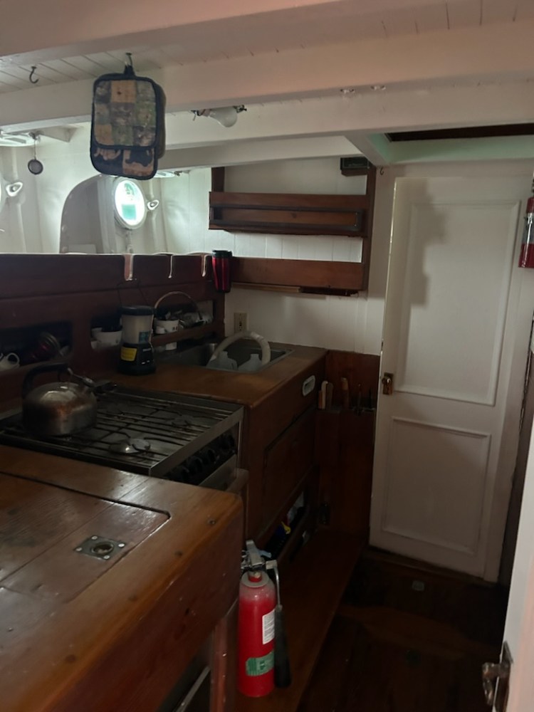Wooden ship kitchen with stove, sink, and fire extinguisher.