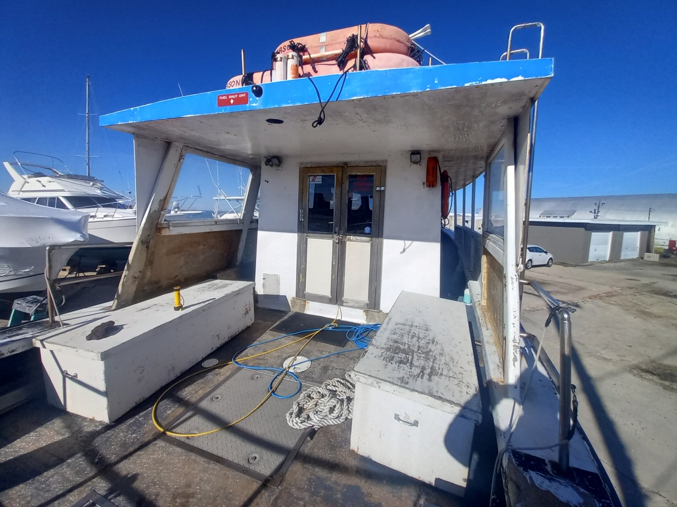 Boat docked, storage boxes on deck, lifebuoy above, clear sky.