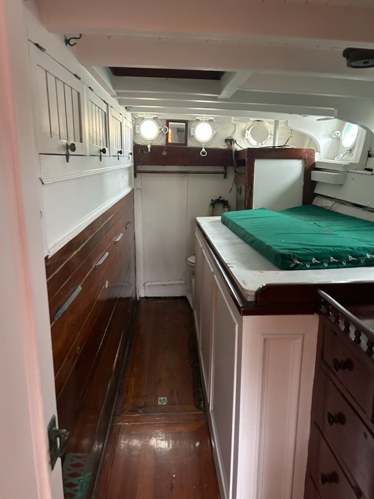 Interior of a wooden boat cabin with green bedding and portholes.