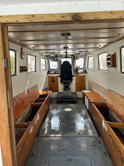 Interior of a small boat cabin with wooden benches and a central steering seat.