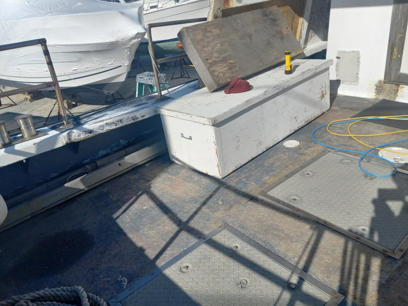 Boat deck with storage bench, rope, and cleaner bottle in sunlight.